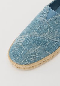 Scarpa slip-on in tessuto blu con motivo a foglia, punta arrotondata piatta e suola in fibra naturale con finitura testurizzata.