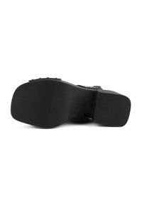 Semelle noire d’une chaussure avec un bout carré et une surface antidérapante texturée, montrant des détails de rivets métalliques le long du bord.