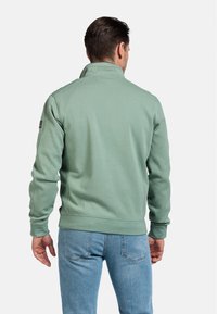 Groene sweatshirt met een hoge kraag, geribde manchetten en onderkant. Zachte stoffen textuur, minimalistisch ontwerp, met een logo-patch op de mouw.