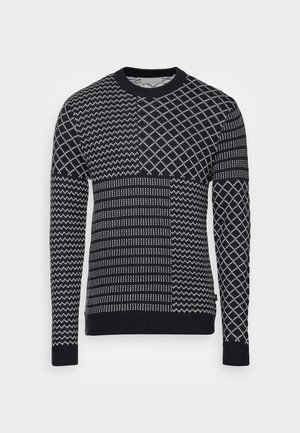 Pull bleu marine présentant des motifs géométriques mélangés en blanc, avec un col rond, des manches longues, des poignets et un ourlet côtelés. Tricot doux et texturé.