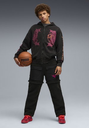 Black zip-up hoodie with pink graphics, paired with black fleece cargo pants featuring pockets and accents; red sneakers, holding a basketball.