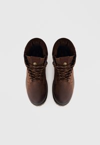 Botas de tobillo de cuero marrón con punteras redondas, ojales de metal y cordones marrones con borde amarillo. Acolchado suave alrededor del collar. Suela de goma texturizada.