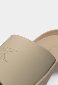 Μπεζ σανδάλι με πλατφόρμα και ανάγλυφο λογότυπο "CK" στο φαρδύ λουρί, με εργονομική σόλα και ανοιχτή μύτη.