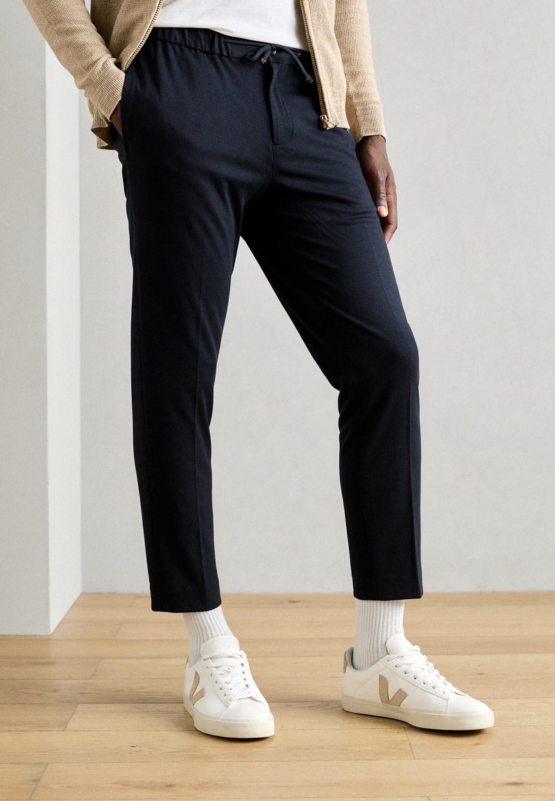 Granatowe spodnie dresowe z elastycznym pasem i sznurkiem do regulacji, o zwężanym kroju. Noszone z białymi trampkami i prążkowymi białymi skarpetkami.