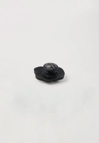Núcleo de goma negra en forma de flor con un centro redondeado, que presenta una textura suave y letras sutiles en la superficie superior.