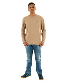 Camicia beige a maniche lunghe con un piccolo logo, abbinata a jeans azzurri chiari e sneakers blu scuro con accenti turchesi.
