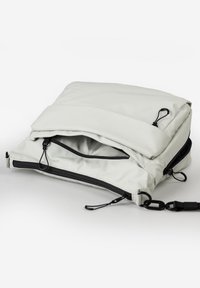 Borsa a tracolla grigia chiara con diversi scomparti neri con cerniera e una tracolla nera removibile su sfondo bianco.