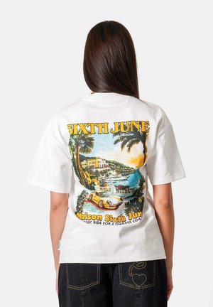 Person with long brown hair wearing a white t-shirt featuring a colorful coastal scene, palm trees, and a yellow sports car graphic.