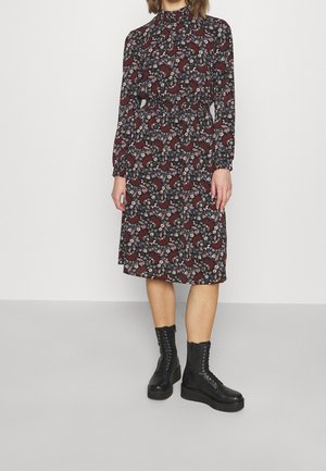 Robe à manches longues à motif floral, col montant, taille cintrée et longueur au-dessous du genou, associée à des bottes noires à lacets.