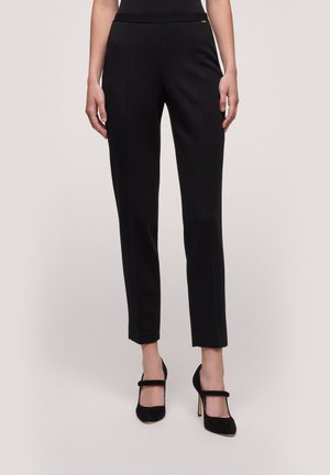 Zwarte op maat gemaakte broek van een gladde stof, met een tailleband met een discrete gouden accenten. Slank model met een cropped lengte.