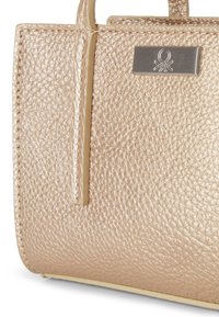 Primo piano di un angolo di una borsa in metallo dorato testurizzato con doppi manici e una piccola placca metallica rettangolare.