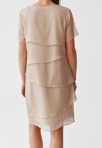 Lyhyt, kerroksellinen mekko pehmeästä beigestä kankaasta, jossa on teksturoidtu, laskostettu muotoilu. Mallissa on lyhyet hihat ja pyöreä pääntie.
