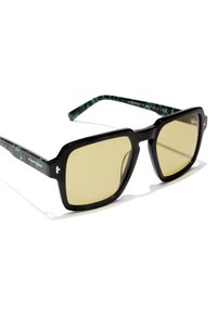 Mustat ylisuuret aurinkolasit keltaisilla sävytetyillä linsseillä. Sangan varret ovat vihreän marmoroidun kuvioinnin kanssa. Kulmikas kehysmuotoilu korostetuilla reunoilla.