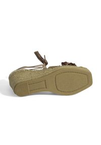 Espadrille Wedge-Sandale mit einer gewebten Jutesohle, beigem Gummiboden und braunen Schleifen, die am Knöchel gebunden sind. Floraler Akzent an der Vorderseite.