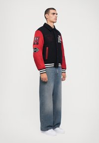 Jachetă varsity neagră și roșie cu broderii, mânici și guler stripe. Asortată cu blugi largi albaștri și adidași albi.