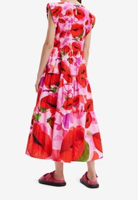 Květinové maxi šaty z růžové látky se vzorem velkých červených rtů; vrstvený design a krátké rukávy; doplněné růžovými botami.