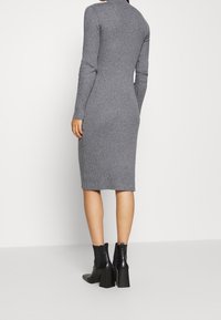 Robe en tricot côtelé gris avec des manches longues et un col haut, silhouette ajustée, se terminant au milieu du mollet, associée à des bottines à talons carrés noires.