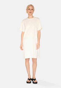 Cream-colored short-sleeve dress with a relaxed fit, made of soft fabric, reaching mid-thigh. Paired with black platform sandals.