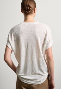 Off-white, locker Sitzendes T-Shirt mit kurzen Ärmeln und rundem Halsausschnitt, aus leichtem Stoff mit einer leicht strukturierten Oberfläche.