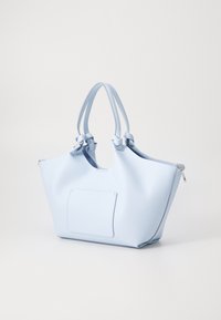 Lys blå totebag med teksturert finish, doble håndtak, glidelås og en frontlomme. Tilbyr et romslig, strukturert design.