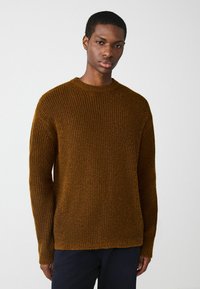 Brauner gerippter Strickpullover mit langen Ärmeln, Rundhalsausschnitt und Seitenschlitzen. Hergestellt aus strukturiertem Material, mit lockerer Passform.