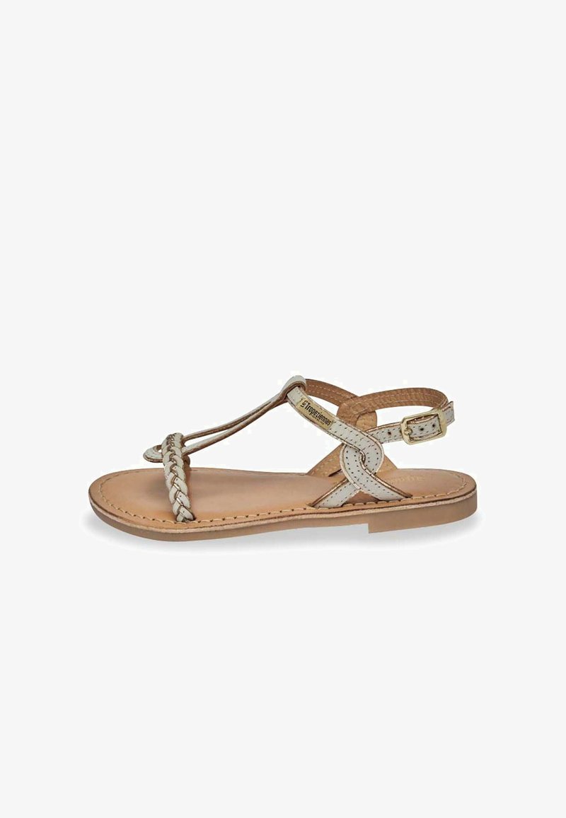 Sandale en cuir tressé avec un dessus beige clair, semelle plate, bride de cheville ajustable et détails cousus sur la base.