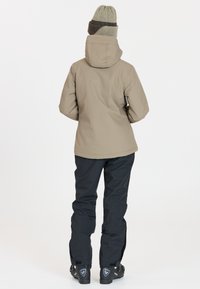 Beige vattentät jacka med huva, tillsammans med svarta byxor och slitstarka svarta stövlar. Jackan har en mjuk textur och en skräddarsydd passform.