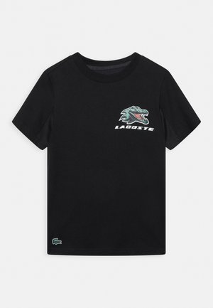 Sort bomulds T-shirt med korte ærmer, der har et grønt krokodillelogo og "LACOSTE" tekst i hvid på venstre side foran.