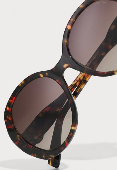 Runde Sonnenbrillen mit Tortoiseshell-Muster, dunklen Gläsern und glänzender Oberfläche. Auffällig sind die dicken Rahmen und die mutigen Designelemente.
