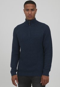 Cárdigan de cremallera en color marino con un patrón de punto texturizado, puños y dobladillo acanalados, presenta un cuello alto y cremallera frontal para un ajuste ceñido.