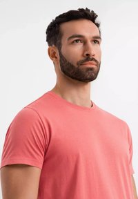 Korálová bavlněná trička s kulatým výstřihem a krátkým rukávem. Hladká textura, klasický střih, minimalistický design a žádné viditelné vzory nebo akcenty.