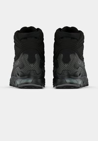 Sapatilhas de cano alto pretas com painéis texturizados, colarinho almofadado e sola transparente, apresentando um design elegante e detalhes refletivos.