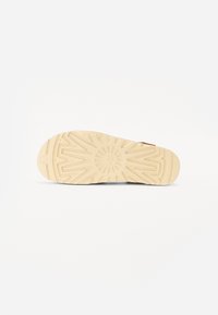 Såle av en sko med en teksturert gummioverflate med et solstrålemønster, farget i beige med en lett buet form.
