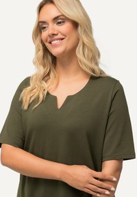 Top verde oliva a maniche corte con scollo a V e dettagli di cucitura discreti sul davanti. Tessuto morbido e liscio con vestibilità rilassata.