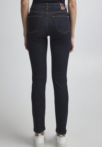 Jeans skinny de denim azul oscuro con una cintura alta, que presentan detalles de costura sutiles, dos bolsillos traseros y un parche de cuero marrón en la cinturilla.