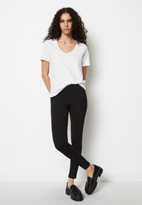 Hvit v-hals t-skjorte paret med svarte tettsittende leggings og store svarte loafers. Glatt tekstur, enkelt design og monokrom fargepalett.