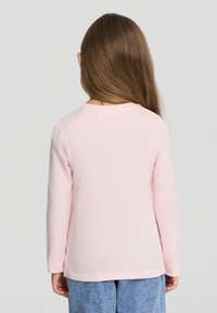 Różowa bawełniana koszula z długim rękawem, okrągłym dekoltem, gładką fakturą i luźnym krojem, w połączeniu z jasnoniebieskimi dżinsami.