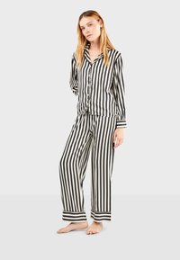 Zwart-wit gestreept pyjama set met lange mouwen en wijde broekspijpen. Voorzien van een knoopshirt en omgeslagen pijpen. Glad textuur.
