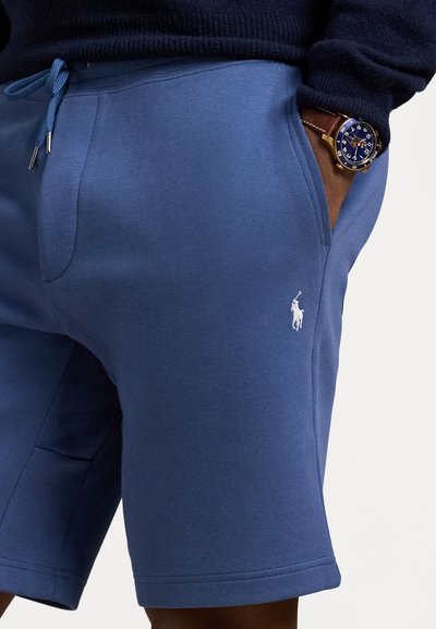 Pantaloni scurți din bumbac albastru cu talie elastică, șnur ajustabil, buzunare laterale și un mic logo brodat pe coapsă. Textură moale.