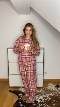 Pink and brown checkered pajama set, long-sleeved shirt and pants with drawstring, soft fabric, worn with beige slippers, holding a white mug.