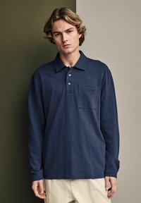 Marineblaue langärmlige Polohemd aus weichem Stoff mit einer Knopfleiste mit drei Knöpfen und einer Brusttasche, locker sitzend und mit geripptem Kragen.