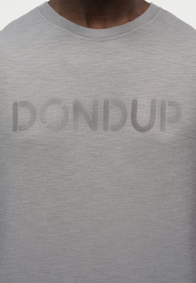 Κοντινό πλάνο ενός ατόμου που φοράει ανοιχτόγριμη μπλούζα με στρογγυλή λαιμόκοψη και διακριτικό λογότυπο "DONDUP" τυπωμένο στο στήθος.