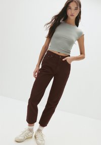 Tricou scurt bleu deschis, pantaloni maronii cu talie înaltă și adidași bej. Material neted, croi lejer și detalii de cusut vizibile.