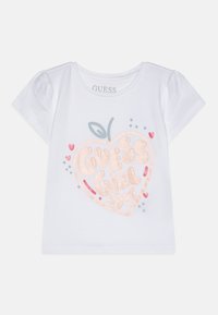 Hvit T-skjorte med korte ermer som har et rosa glitrende hjertegrafikk og teksten "GUESS Girl 1981", akkompagnert av små fargede prikker og hjerter.