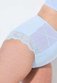 Helle blaue Unterwäsche aus einem weichen, glatten Stoff mit einem Spitzenüberzug und gewelltem Rand, ergänzt durch transparente Netzdetails.