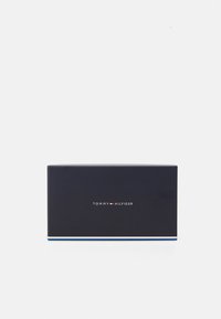 Tommy Hilfiger gift box, rectangular, dark blue with white and red logo text. Features a subtle striped accent at the bottom. Matte finish.