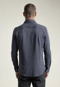 Camisa de manga larga azul marino con cuello con solapa, puños abotonados y pliegue trasero. Textura suave y ajuste entallado con dobladillo redondeado.
