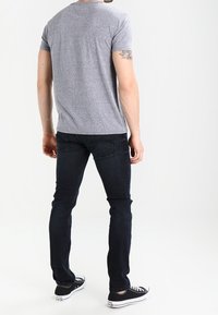 Šedé tričko s krátkým rukávem a kulatým výstřihem, v kombinaci s tmavými džíny. Pohodlné černé tenisky s bílou podrážkou a tkaničkami.