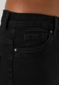 Jean en denim noir avec une taille mi-haute, un design à cinq poches, une légère décoloration et des accents en métal pour plus de durabilité.