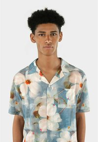 Kortärmad skjorta i lätt, genomskinlig tyg med blå bakgrund, som har stora vita blommönster och en bröstficka.